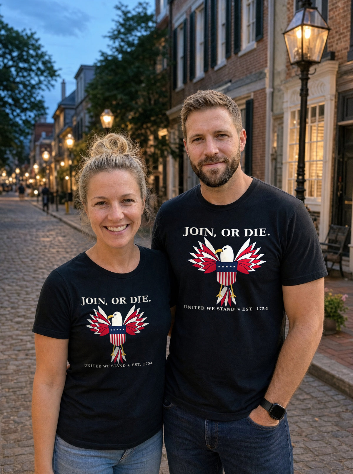 Couple in black Join, or Die eagle tees on a cobblestone street at dusk