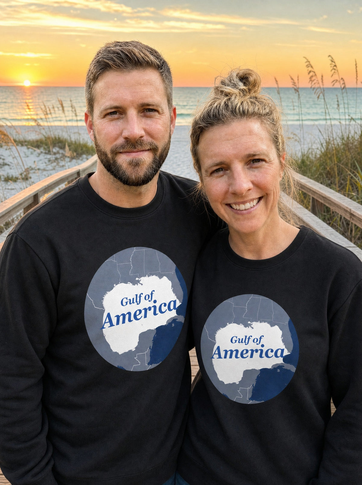 Garrett and Savannah wearing matching black Gulf of America retro map sweatshirts on a beach boardwalk at sunset