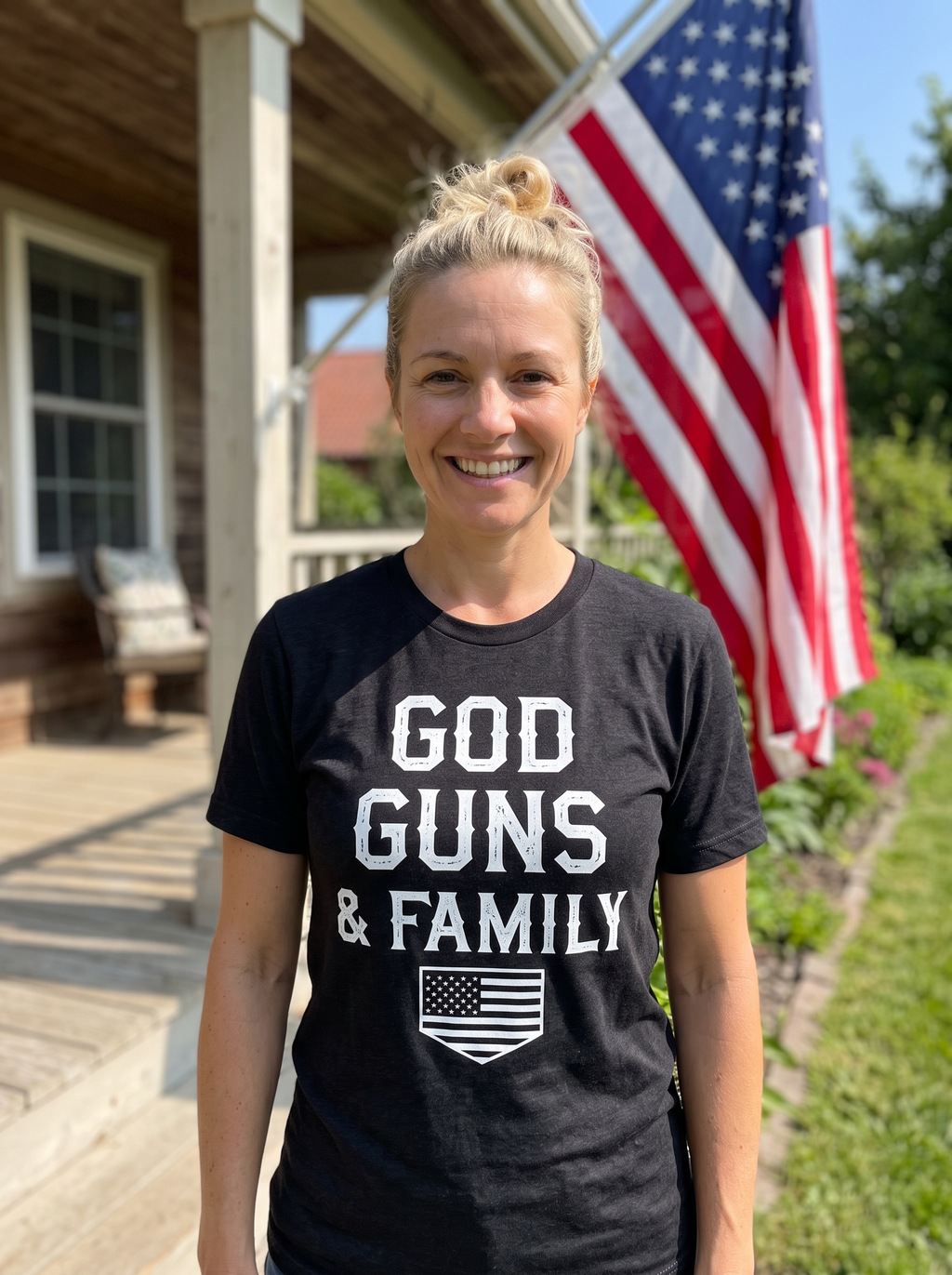 Woman wearing the black heather God, Guns, & Family Classic Tee with white lettering and American flag shield on a farmhouse porch