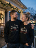 Couple in black Joy to the World Christmas crewneck sweatshirts on a decorated porch at dusk (AI-generated)