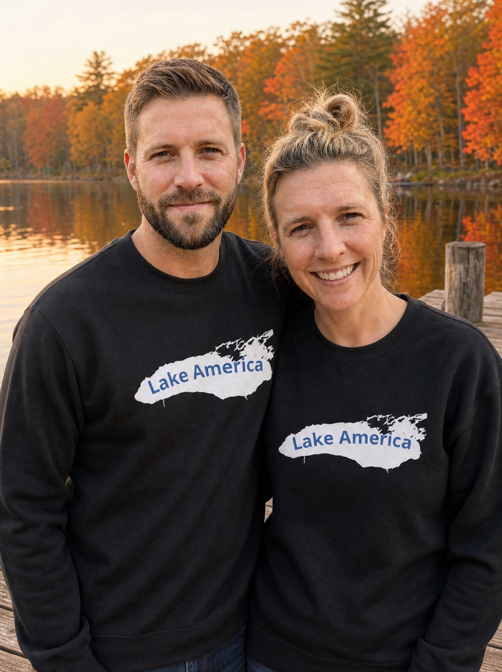Couple in black Lake America crewneck sweatshirts standing on an autumn lakeside dock