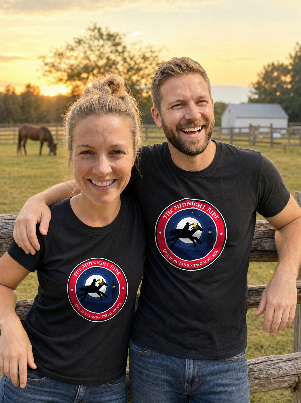 Couple in black Midnight Ride 1775 badge tees standing at a pasture fence at sunset