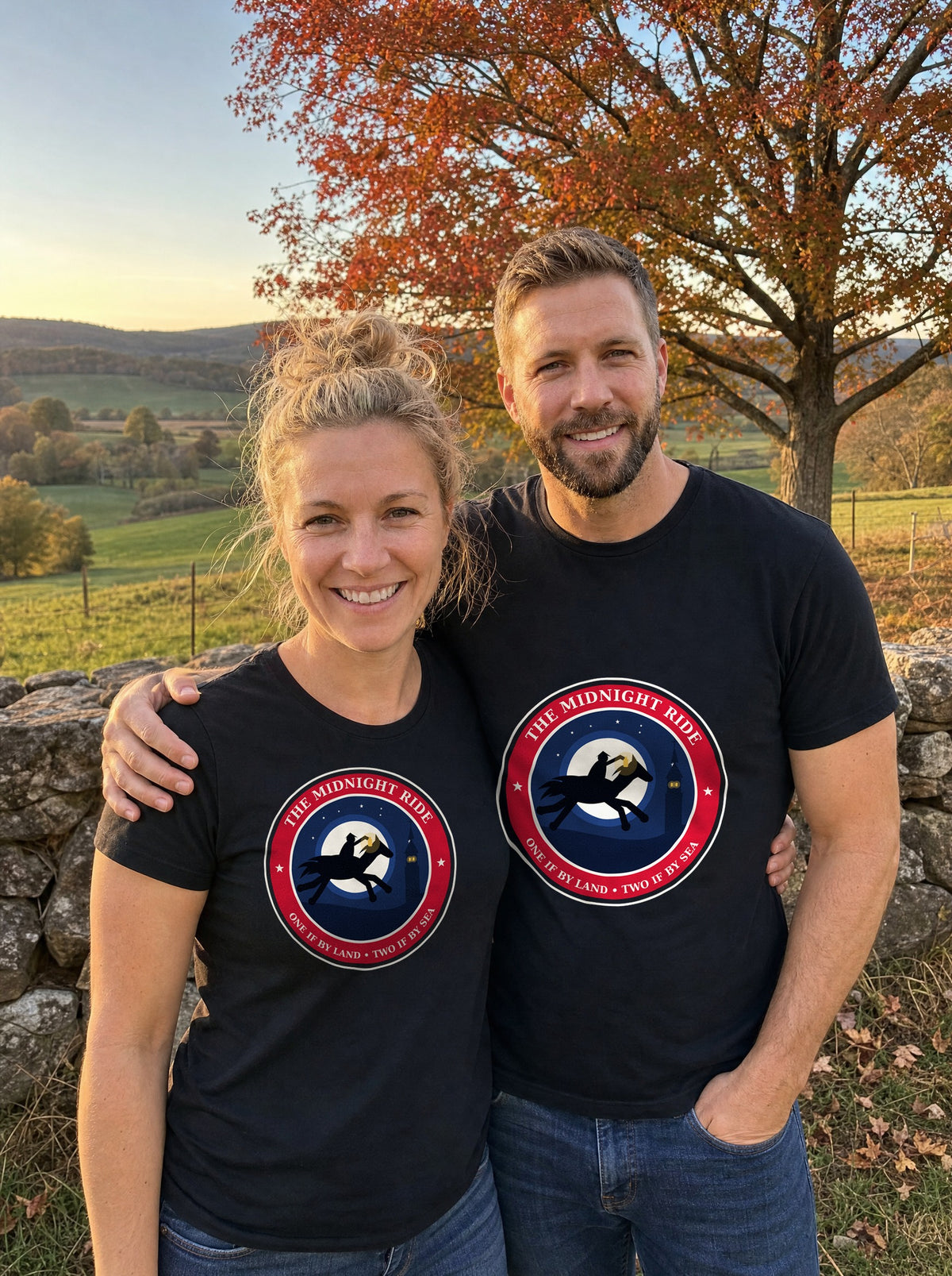 Couple in black Midnight Ride 1775 badge tees standing by a stone wall in autumn