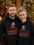 Garrett and Savannah wearing matching Mr. Claus and Mrs. Claus Patriot Edition black Christmas hoodies in front of a lit Christmas tree and fireplace