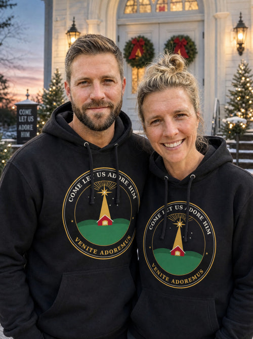 Garrett and Savannah wearing matching black Come Let Us Adore Him Nativity badge hoodies on the steps of a decorated white church at Christmas dusk