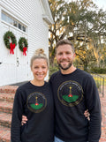 Man and woman in black Come Let Us Adore Him Nativity badge sweatshirts standing on church steps with Christmas wreaths
