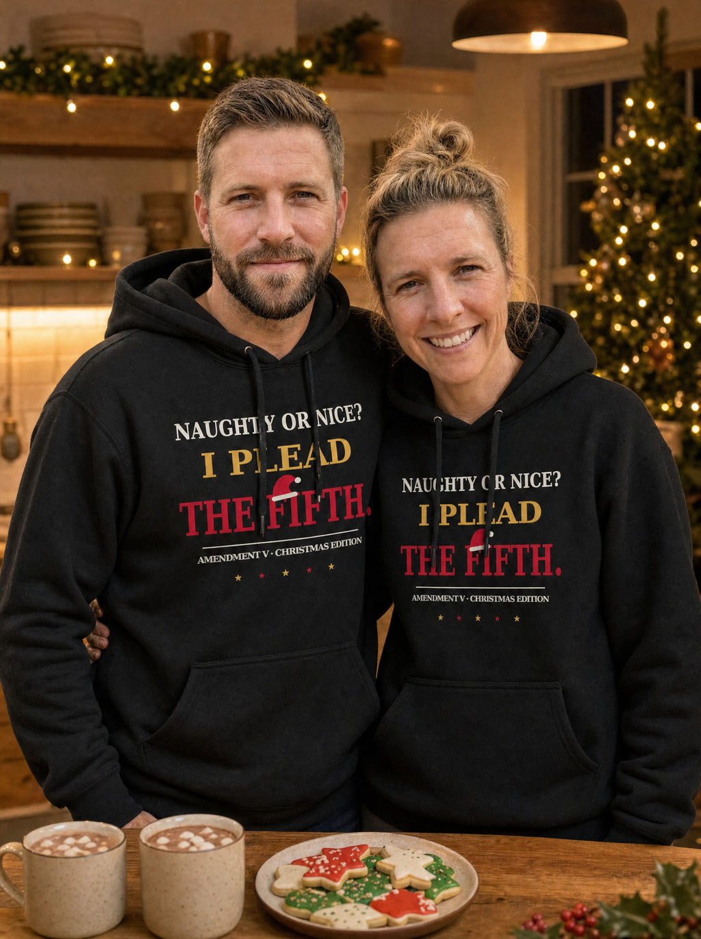 Garrett and Savannah in matching black I Plead the Fifth Christmas Edition pullover hoodies with a Santa hat graphic, standing at a kitchen island with hot cocoa and sugar cookies
