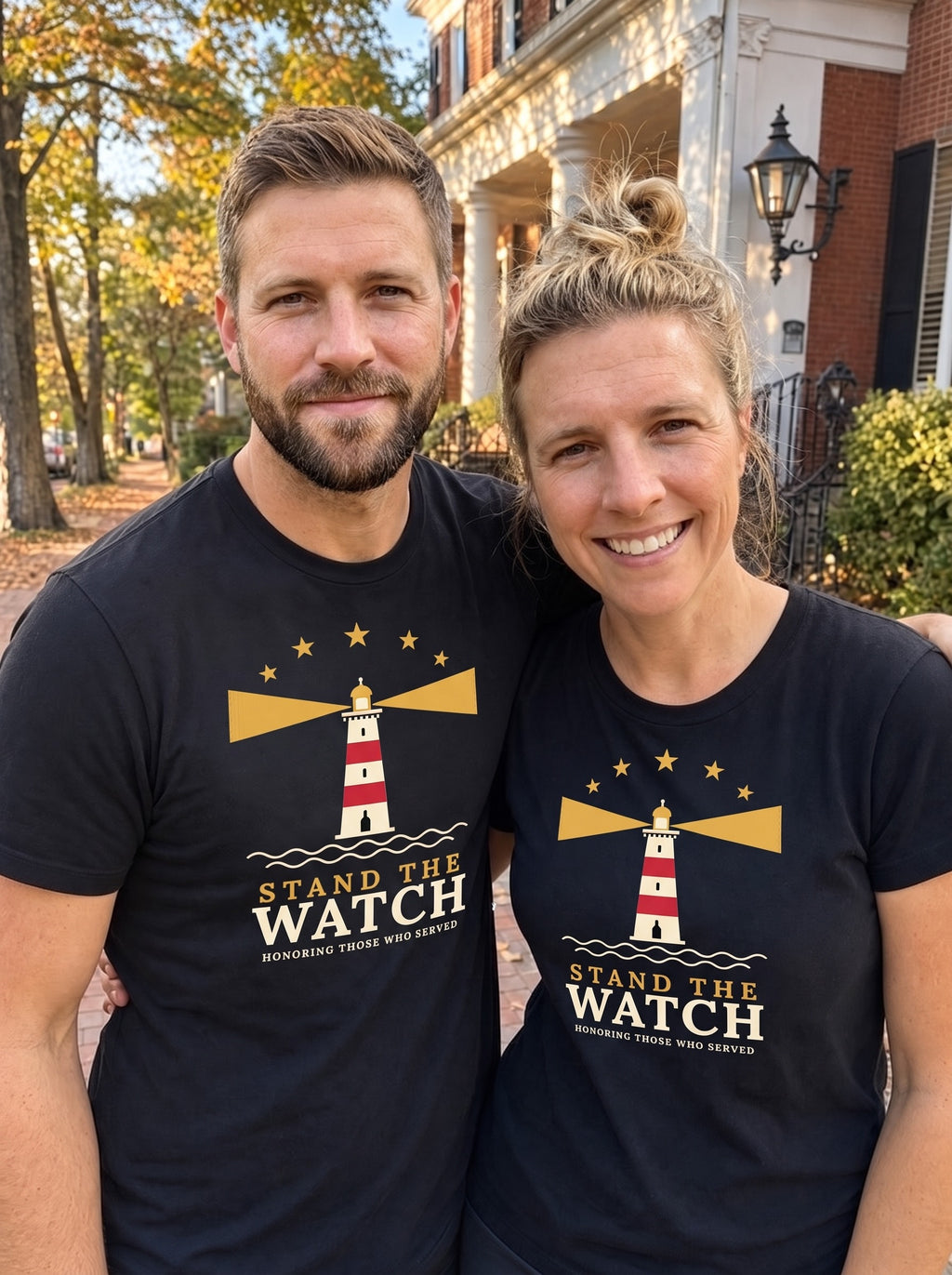 Couple wearing matching black Stand the Watch lighthouse tees on a brick street (AI-generated image)