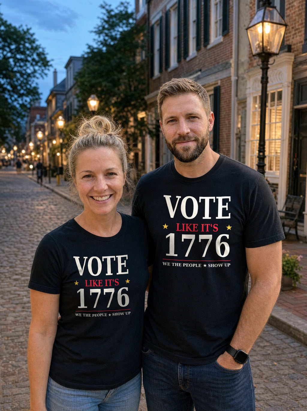 Couple in black Vote Like It's 1776 tees on a cobblestone street at dusk